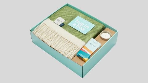 A turquoise card gift box with a green blanket, candle and box of chocolates