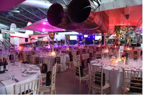 A conference room with an aeroplane hanging from the ceiling wtith lots of tables set for food