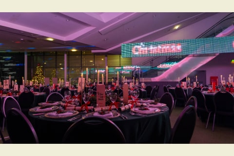 A room dressed with dining tables with crackers and candles on the tables and a sign with Christmas written in lights