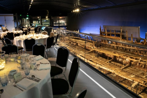 A room with the remains of a sailing boat on one side and tables set for dinner on the other side