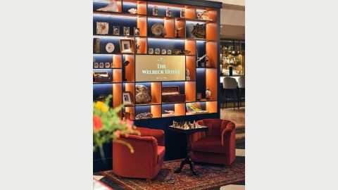 Two bucket chairs around a small table in front of a divider shelf full of objects with a bar behind