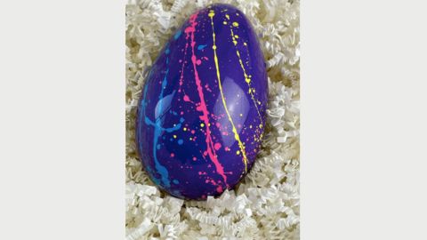 A dark blue coloured easter egg with pink, yellow and light blue lines on it on top of white pieces of paper
