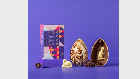 A milk and white chocolate easter egg cracked in two with one half showing marbling detail and the second with a white chocolate dinosaur inside