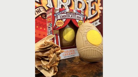 A golden chocolate easter egg leaning against a red box with broken easter egg pieces next to it