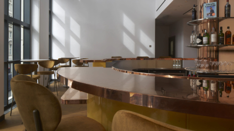 A shiny copper circular bar with high backed seats and bottles on the shelves behind.