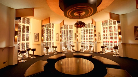 Circular seating around a circular table. In the background are stools set within five art deco curved window recesses. A large circular light fitting hangs from the ceiling.