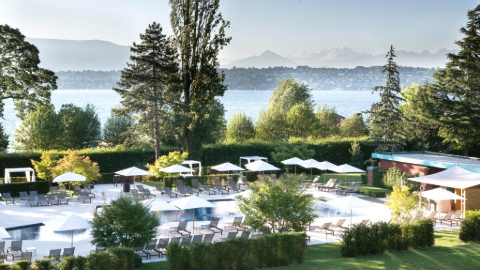 The outdoor pool surrounding by grass and trees, with views across Lake Geneva and the mountains