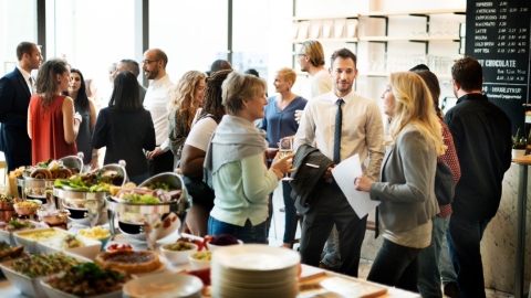 More than a dozen people of different ages networking in a coffee shops, with a large buffet in the foreground.
