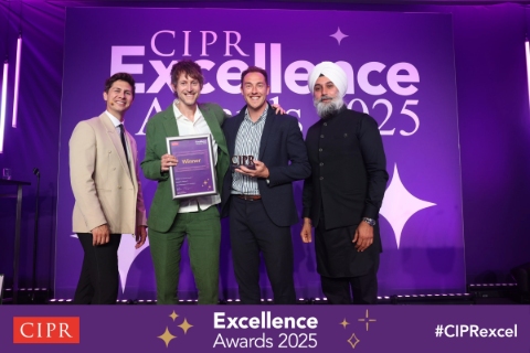 Four men stand on the purple lit CIPR Excellence awards stage.