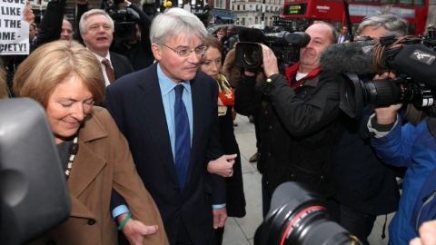 Amid a throng of camera operators and photographers Andrew Mitchell holds his wife's hands while crowds on the pavement gather behind