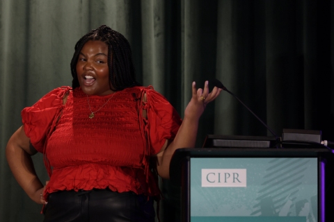 Kira Matthews on stage in front of a green curtain and a lectern with CIPR branding