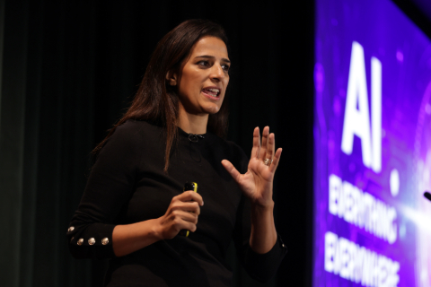 Priya Lakhani on stage with a purple screen displaying the words AI on the right