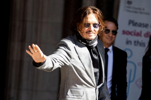 Johnny Depp wearing sunglasses and a grey suit, waves while outside the Royal Courts of Justice