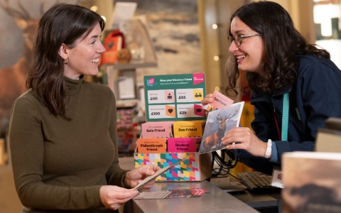 Two smiling white women with dark hair and dark clothing chatting over a counter which features a display of various gift cards