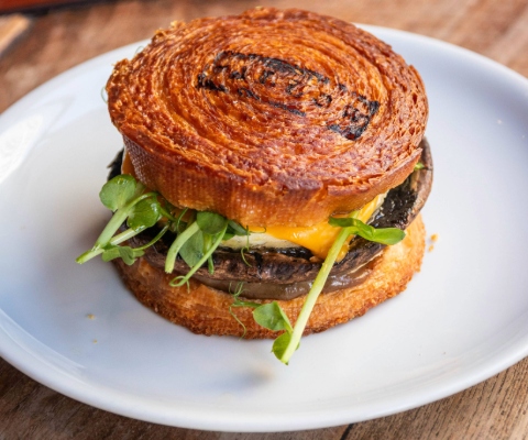 A circular croissant filled with mushroom, watercress and egg on a white circular plate.