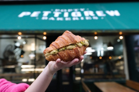 An arm holding up a pistachio filled croissant outside Pettigrew Bakery