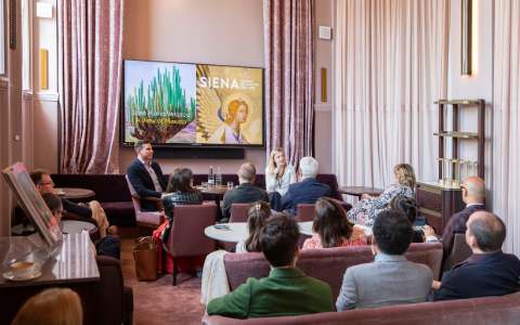 A presentation on the artist Siena to a group sat on sofas in a pale pink room with high ceilings.