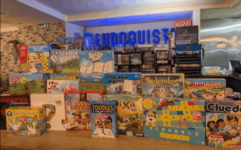 A selection of board games lined up on a table with a neon blue light in the background that spells Ludoquist