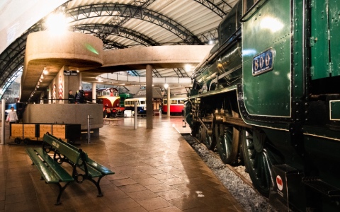 Side of a green train next to a green bench with more train carriages in the background
