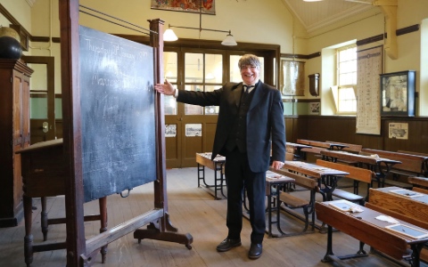 A classroom with a blackboard and a teacher dressed in a Victorian teaching uniform