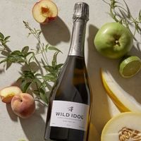 A dark sparkling wine bottle surrounded by fruit.